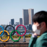 Un homme portant un masque marche devant les anneaux. olympiques à Tokyo.