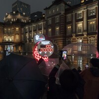 Une foule rassemblée sous des parapluies observent dans la pénombre le cadran indiquant le nombre de jours avant les Jeux olympiques de Tokyo.