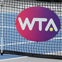 Les lettres WTA écrites en blanc sur un fond rose et mauve et fixées à un filet de tennis.
