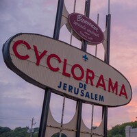 L'affiche ovale du Cyclorama de Jérusalem devant un soleil couchant.