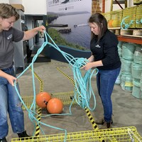 Deux employées démêlent une corde rattachée à une cage en métal.