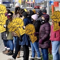 Des grévistes alignés sur le trottoir. Ils ont des masques sur le visage à cause de la pandémie et brandissent des affiches jaunes en forme de poing levé.