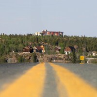 Une route avec deux traces jaunes et au fond de vieux bâtiments dans la forêt boréale