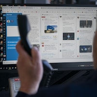 Un homme décroche le combiné d'un téléphone en faisant face à un écran d'ordinateur allumé.