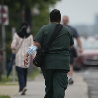 Une femme marche dans la rue, un masque médical attaché à son coude.