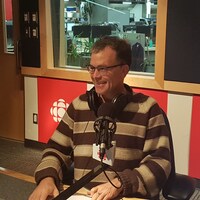 Un homme est dans un studio de radio, assis devant un microphone.