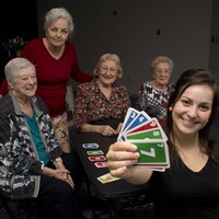 Autour d'une table noire, trois aînées et une étudiante jouent aux cartes. 