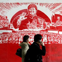 Deux personnes passent devant l'affiche qui représente le leader Mao Zedong souriant devant une foule de travailleurs.