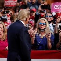 Donald Trump de dos, devant des partisans. Il fait un signe de pouce en l'air à une femme, qui fait la même chose.