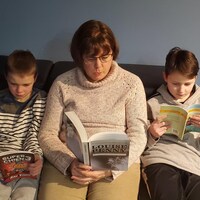 une dame et deux enfants assis sur un canapé, un livre à la main.