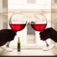Deux personnes lèvent un toast avec leurs coupes de vin rouge.