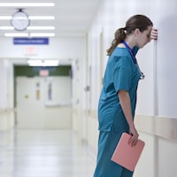 Une professionnelle de la santé est appuyée contre un mur dans un couloir d'hôpital.
