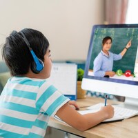 Un garçon devant un ordinateur assiste au cours donné par son enseignante.