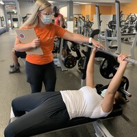Une entraîneuse dans une salle de sports qui accompagne une cliente sur un équipement de musculation. 