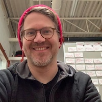 Dominic Desjardins, scénariste et réalisateur chez Zazie Films portant un bonnet rouge devant un tableau couvert de post-it