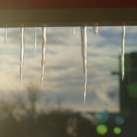 Gros plan sur des pics de glace devant une fenêtre, un matin d'hiver ensoleillé.