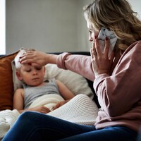 Une mère met une main sur le front de son fils pour prendre sa température, tout en portant son téléphone à l'oreille de l'autre main. 