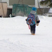 Un enfant marche dans la neige avec son sac d'école.