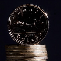 Un dollar canadien en équilibre sur une pile d'autres sous.