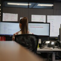 Une femme de dos assise devant un ordinateur.