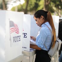 Une électrice consulte un document derrière un isoloir.