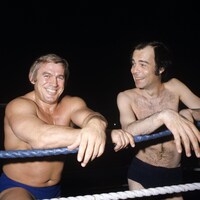 Sur un ring, le lutteur Édouard Carpentier et l'animateur Jacques Fauteux sont debout, les bras appuyés sur les câbles qui forment un côté du ring.