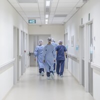 Quatre employés médicaux marchent de dos dans un couloir d'hôpital.