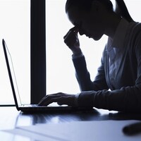 Les yeux fermées et exténuée, une travailleuse prend une pause devant son ordinateur portable. 