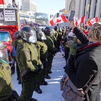 Des policiers portants des casques font face aux manifestants dans le centre-ville d'Ottawa. 