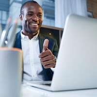 Une personne sourit et lève son pouce de la main gauche devant son écran d'ordinateur.