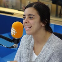 Une femme sourit en parlant devant un micro orange dans un studio de radio. 
