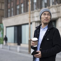 Un jeune homme marche dans la rue avec un café pour emporter dans la main.