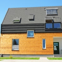 Une maison moderne en bois, avec un toit de couleur foncée et un panneau solaire.