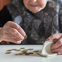 Un dame âgée compte ses sous, posés sur une table devant elle. 