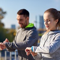 Deux sportifs à l'extérieur consultent leur bracelet connecté.