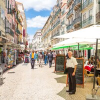 Un serveur se tient devant des terrasses de restaurants dans une rue de Lisbonne.