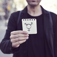 Une personne tient un papier sur lequel est dessiné le symbole transgenre.