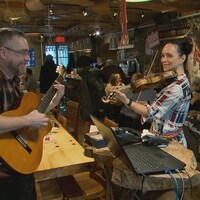 Un homme joue de la guitare et une femme joue du violon dans un restaurant, devant les clients.