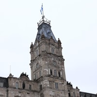 Gros plan sur la tour centrale de l'édifice sur laquelle le drapeau du Québec flotte sur un mât.