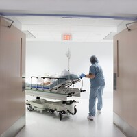 Une infirmière pousse un patient sur une civière à travers les portes menant à un corridor dans un hôpital.