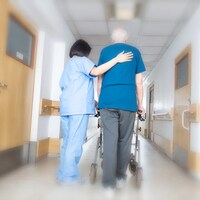 Une infirmière aide un homme à marcher dans le couloir d'un centre de soins.