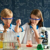 Un garçon et une fille portant des lunettes de laboratoire en train d'étudier des réactions chimiques dans des éprouvettes remplies de liquides de différentes couleurs.
