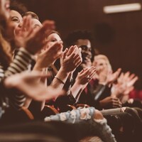 Des spectateurs applaudissent dans une salle de théâtre.