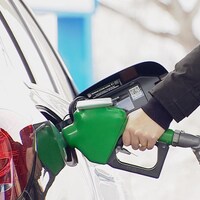 Une main tient une pompe à essence dans une voiture. L'Alberta taxera davantage les émissions de carbone dès janvier.