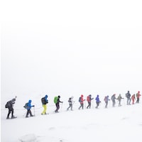 Une trentaine de personnes en raquettes se suivent en file dans une tempête de neige.