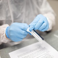 Des mains gantées déchirent un emballage de plastique dans lequel se trouve une cartouche servant au dépistage de la COVID-19.