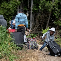 Une famille transporte des bagages alors qu'ils traversent la frontière pour demander asile au Canada.