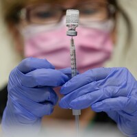 Une infirmière portant un masque et des gants prépare une dose de vaccin.