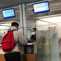 Une agente de l'ASFC portant un masque de protection vérifie le passeport d’un passager.