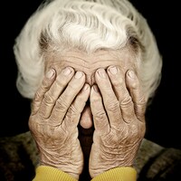 Une dame âgée se couvrant les yeux de ses mains.